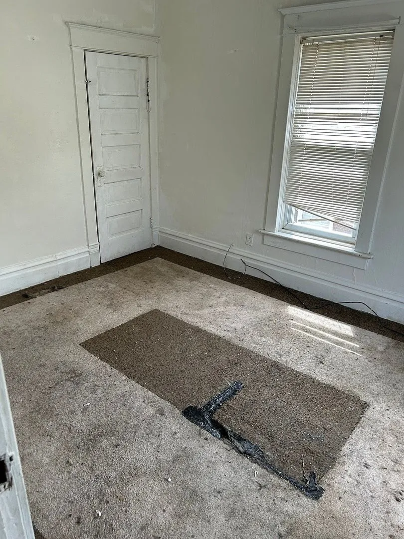 Room with patched carpet and worn floors, 1906 Zion four-square